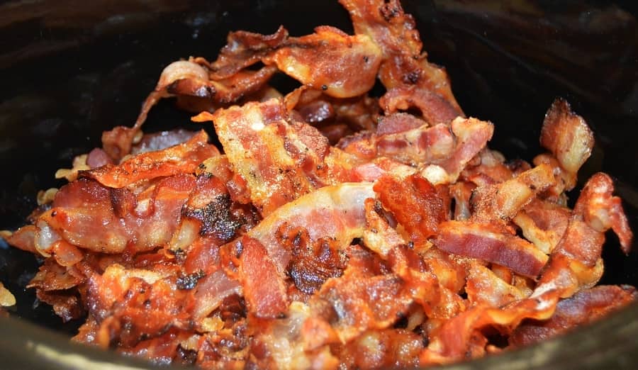 A pile of crispy bacon strips, perfected using a select wood selection for smoking, in a black container.