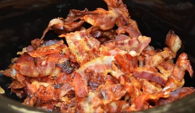 Crispy bacon strips piled in a black dish, fresh from the skillet, highlighting the flavors from our specialized Meat Smoking Chart.