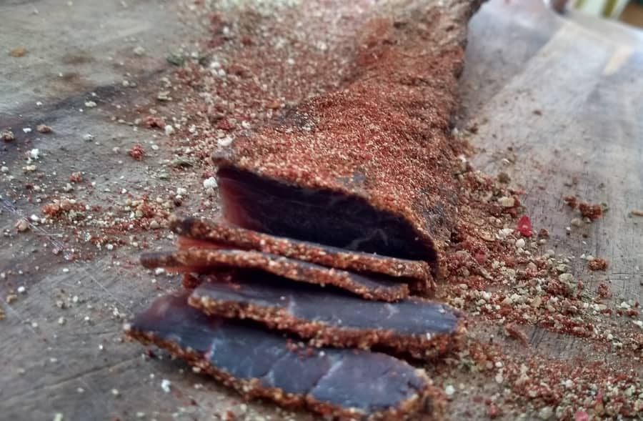 Thinly sliced cured meat with a sprinkle of spices on a wooden cutting board.