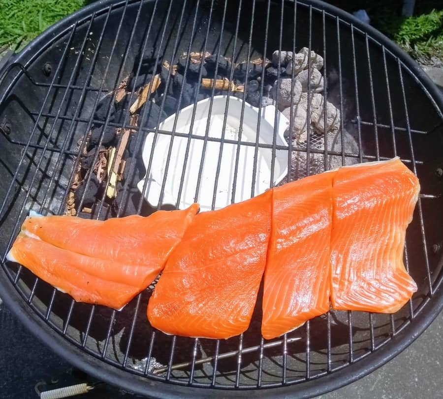 Hot Smoked Salmon fillet on a round Charcoal Kettle Hot Smoker using the 'snake method' for heat, with charcoal and wood chunks burning in a domino style.