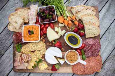 A delectable charcuterie board with an assortment of cheeses, cured meats, fresh fruits, dips, and crackers, arranged on a rustic wooden board, ready for a delightful picnic or gathering.