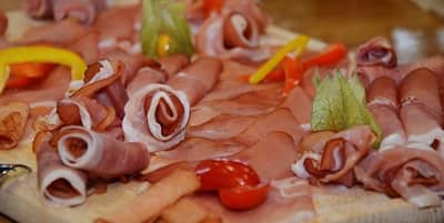 A Charcuterie Board featuring an assortment of thinly sliced cured meats elegantly arranged on a platter, garnished with colorful slices of bell peppers and cherry tomatoes.