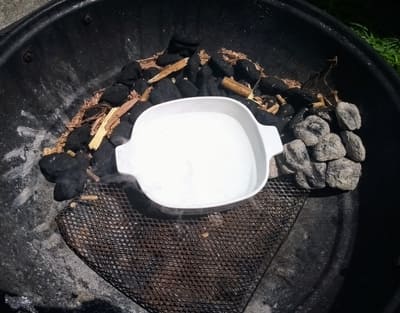 A white bowl surrounded by charcoal and wood chips inside a barbecue grill, waiting for the flames to light up a cookout.