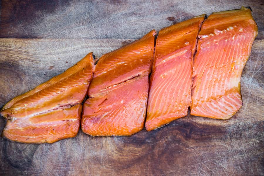 Sliced smoke salmon arranged neatly on a wooden cutting board.