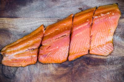 Slices of smoked salmon, prepared using quick easy salmon smoking methods, arranged on a wooden board.