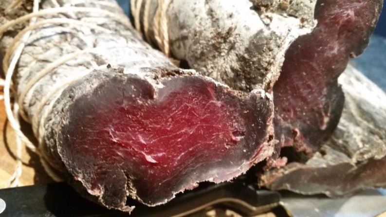 A close-up of sliced cured meat exhibiting a rich, deep red color with a marbled texture, indicative of the main ingredients in high-quality charcuterie.