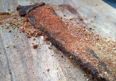 A well-seasoned piece of jerky, a result of curing meat, on a wooden board, with spices scattered around.