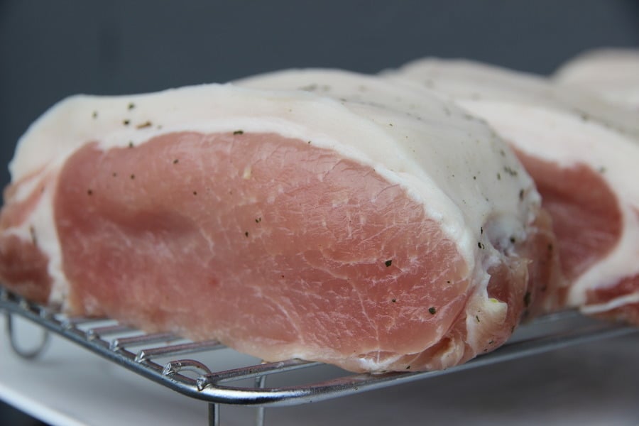 A close-up of a raw, seasoned pork roast with a layer of fat on a metal cooking rack, ready for hot smoking.