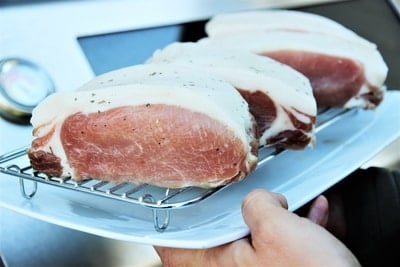 Dry-aged beef steaks covered in a white fat cap being weighed on a kitchen scale, showcasing the preparation of gourmet meat.