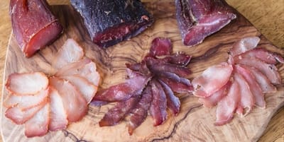 Artisanal cured meats sliced and elegantly displayed on a wooden cutting board.