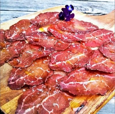 Sliced cured meats arranged on a wooden board, garnished with a small bunch of grapes, ready to be enjoyed as a charcuterie appetizer.