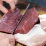 Rectangular Fresh meat being sliced in half on a chopping wooden board