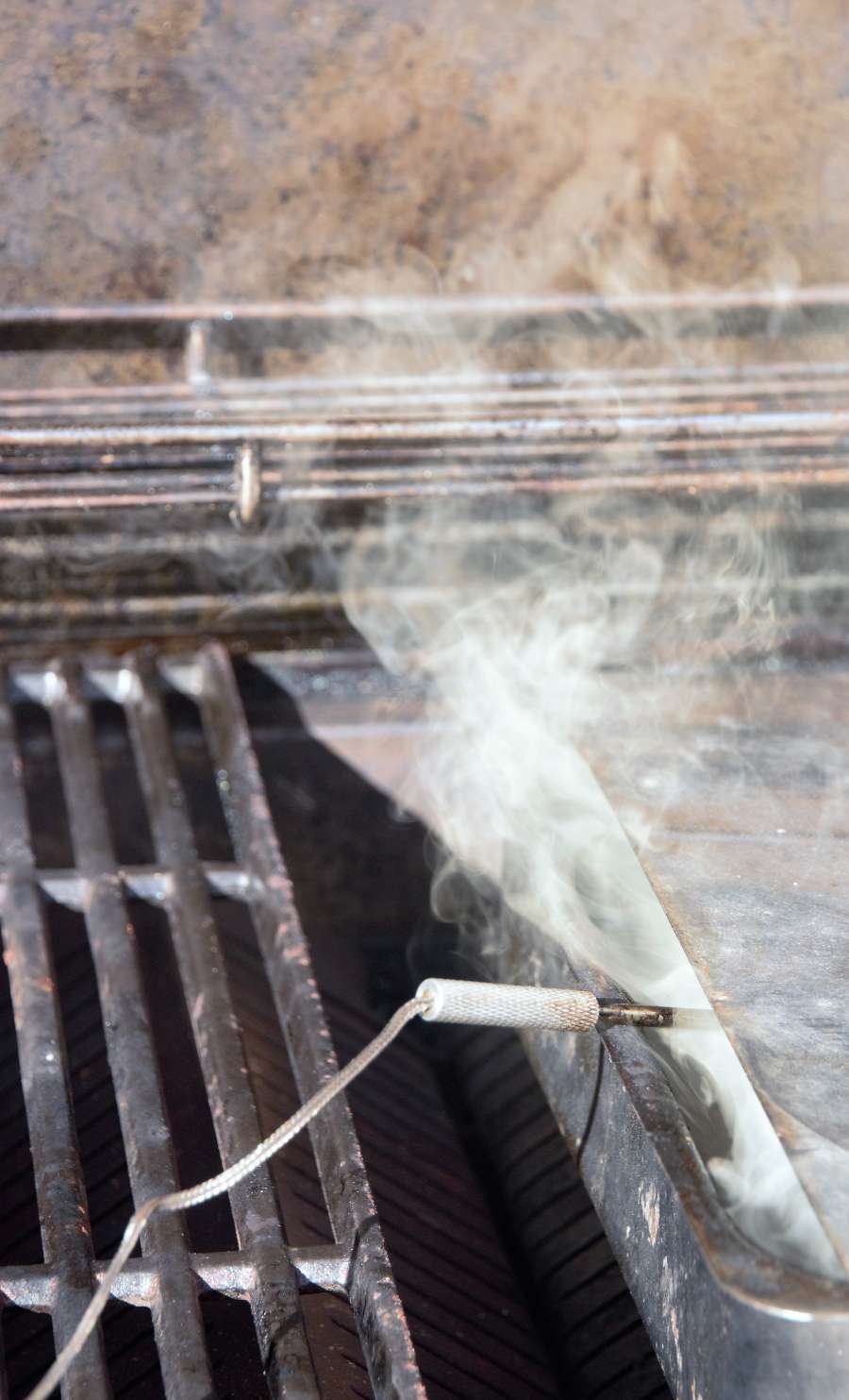 A close-up of a steaming grill with smoke rising, indicating something is cooking or the grill is being preheated.
