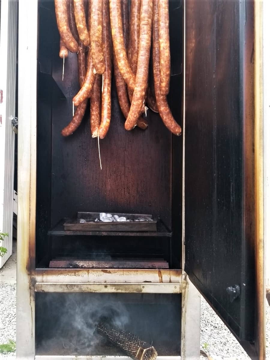 Sausages hanging in a smokehouse, slowly infusing with flavor as they cure over smoldering wood chips.