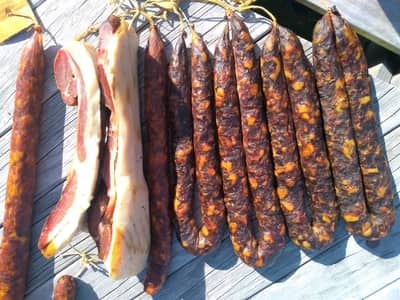 Traditional smoked meats and sausages undergoing cold smoking and drying in the sun for food preservation.