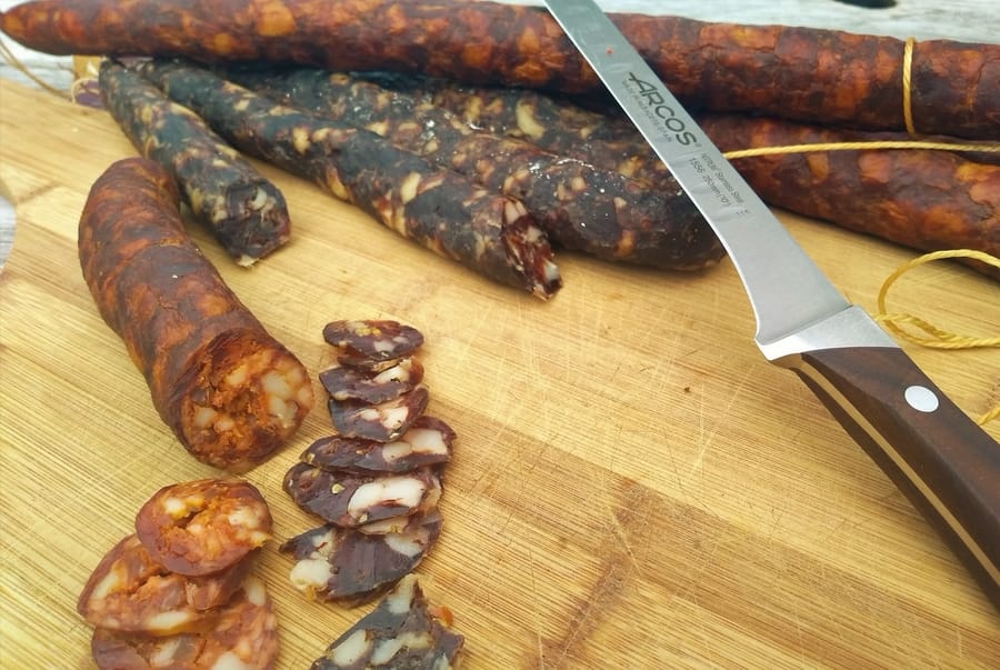 Dry cured salami on a chopping board with a flexible knife on the foreground. Orange and dark brown salami colours.