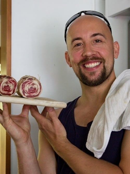 A smiling person proudly displaying a cutting board with fresh radicchio heads in a kitchen setting.