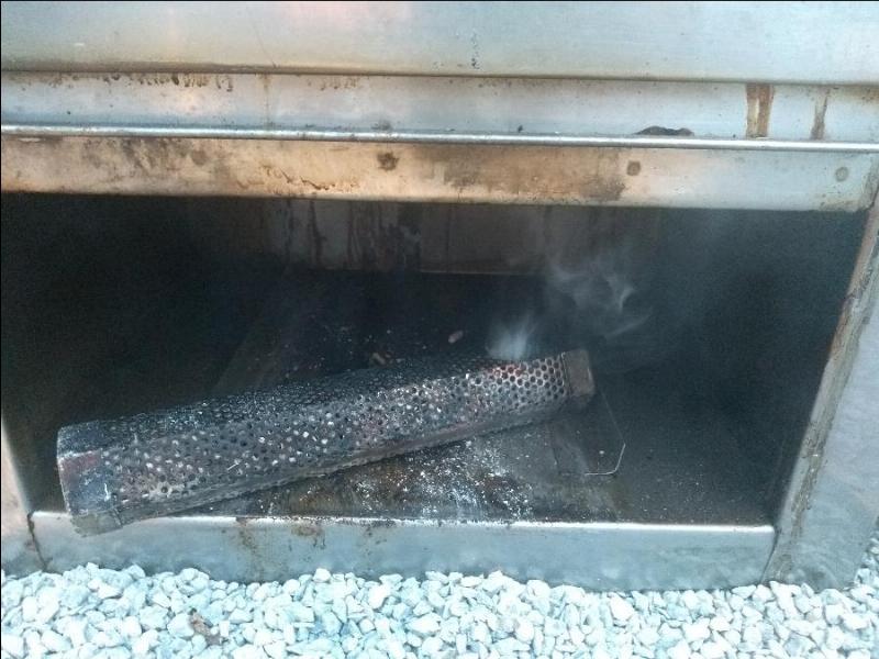 A smoldering pellet tube emitting smoke inside a metal outdoor portable cold smoking round perforated metal tube.