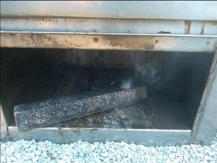 A smoldering log emitting wisps of smoke inside an outdoor grill or firebox, hinting at the remnants of a fire.