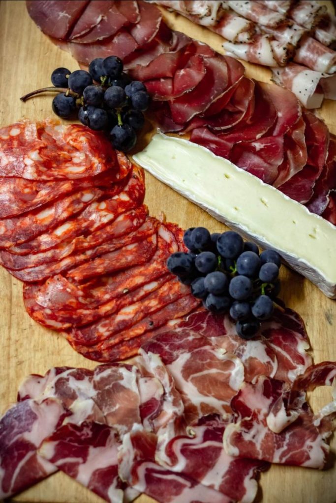 An appetizing charcuterie board featuring an assortment of cured meats, a wedge of brie cheese, and clusters of dark grapes, all artfully arranged on a wooden surface.