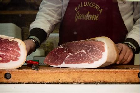 A butcher in an apron prepares to slice a large piece of cured ham on a wooden counter.