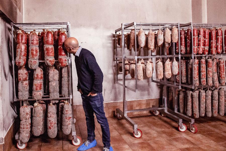 A man intently inspects a rack full of curing meats, possibly checking the quality or progress of the curing process.