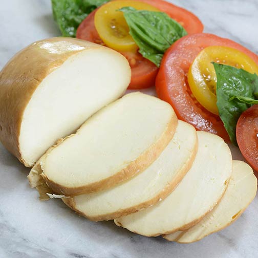 Freshly sliced cold smokers mozzarella cheese with a vibrant tomato and basil salad in the background.