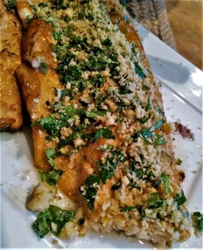 Savory grilled trout topped with finely chopped herbs and a sprinkle of crumbled cheese, served over a bed of seasoned rice.