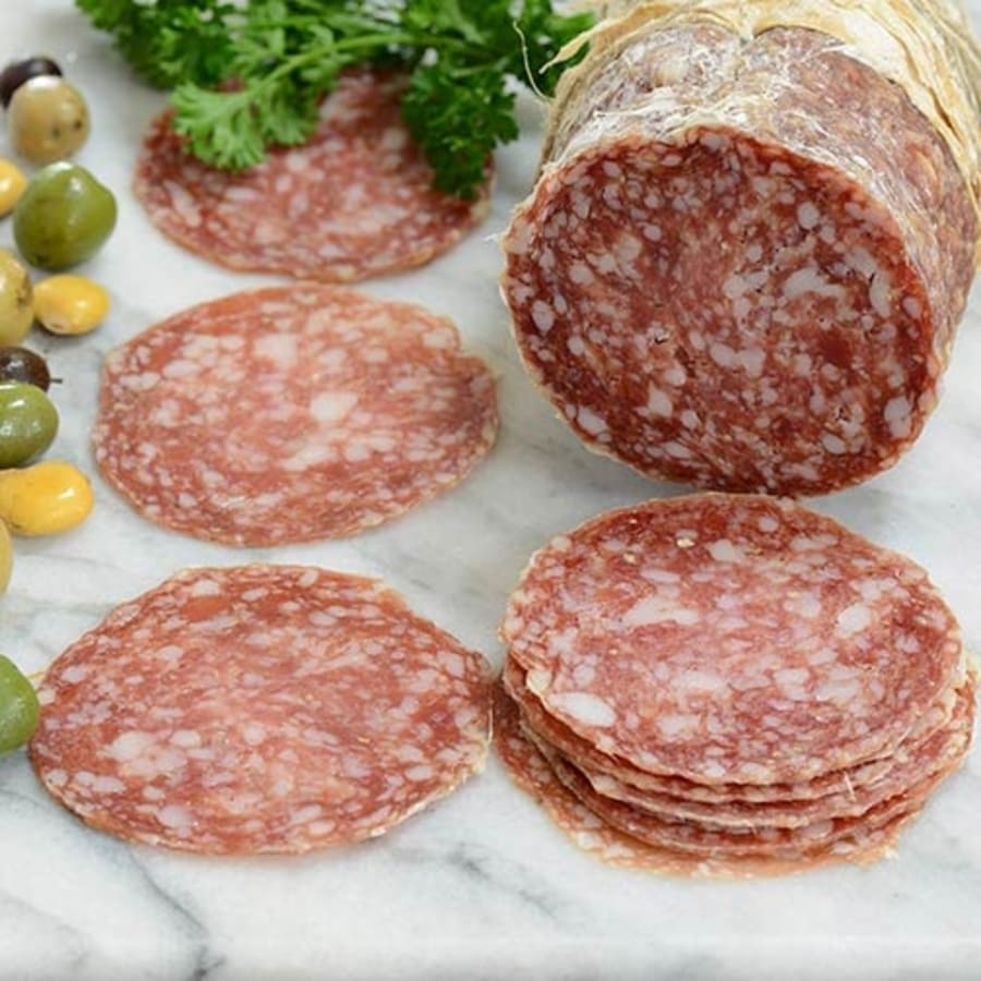 A selection of thinly sliced artisan salami arranged next to a whole artisan salami, with green and yellow olives and parsley garnish on a marble surface.