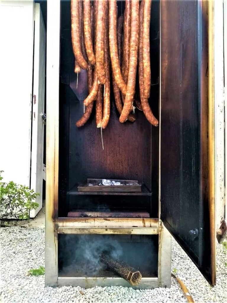 Smoked sausages hanging in a traditional smoking cabinet with wisps of smoke signaling delicious flavors in the making.