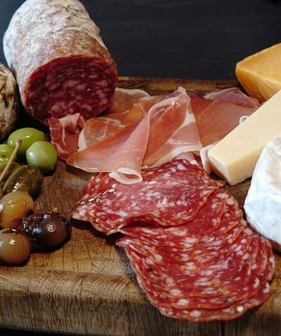 An assortment of gourmet charcuterie and cheeses, featuring slices of salami, prosciutto, and a variety of olives on a wooden board, ready for a savory feast.