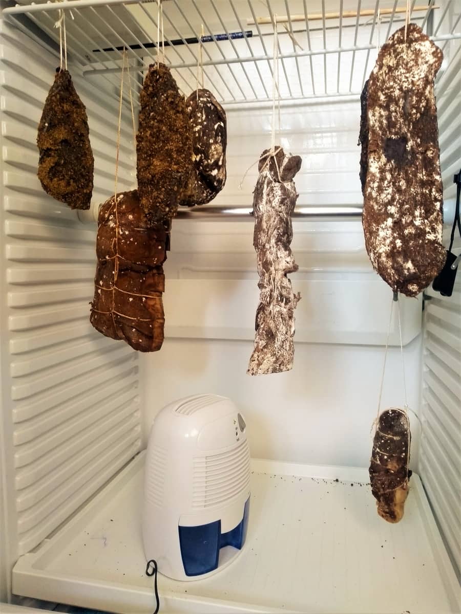 Cured meats hanging to dry in a controlled environment with a dehumidifier to maintain optimal air quality.