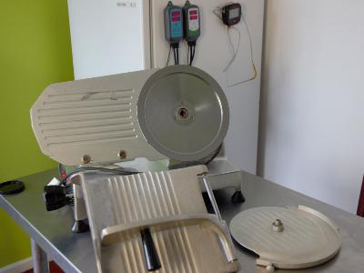 A commercial meat slicer on a countertop in a kitchen setting with its blade guard open, revealing the circular blade, ready for cleaning or maintenance.