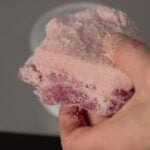 A hand holding a chunk of pink salt crystals, highlighting their texture and color.