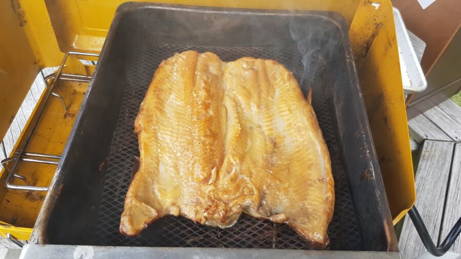 Two large fish fillets grilling on an outdoor barbecue, with smoke rising from the cooking surface.