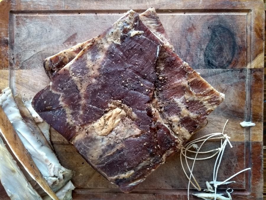 Cured meat with good molds resting on a wooden cutting board with bones and sinew to the side.