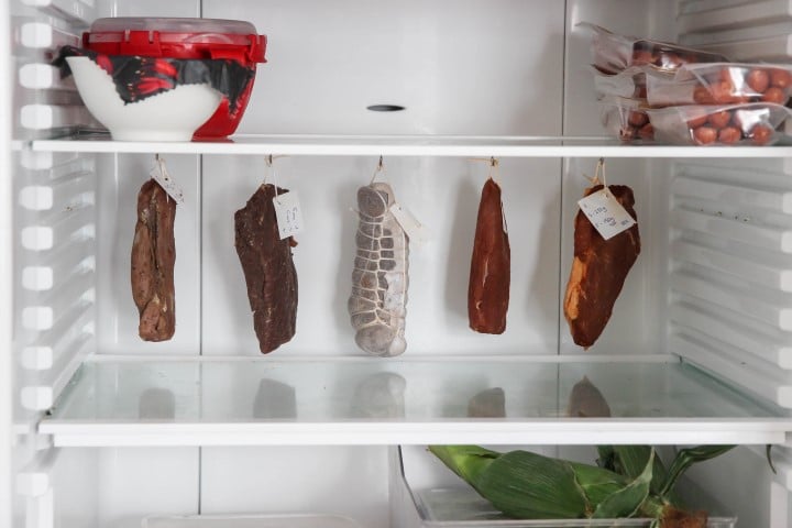 Various types of preserved meats hanging inside a refrigerator, exhibiting the process of aging or storage for flavor development.