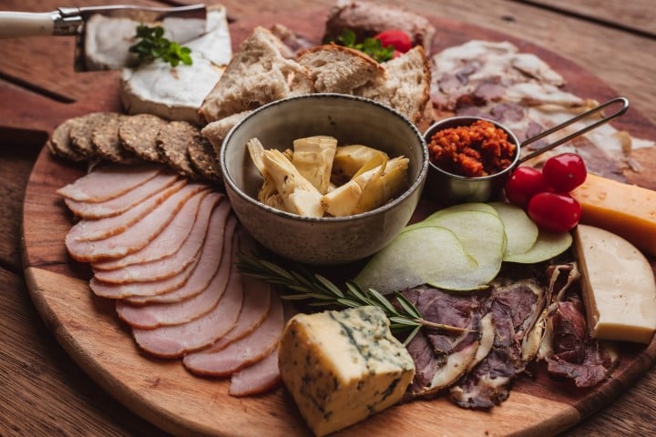 A delectable charcuterie board featuring an assortment of meats, cheeses, bread, and accompaniments, artistically arranged on a wooden serving platter.