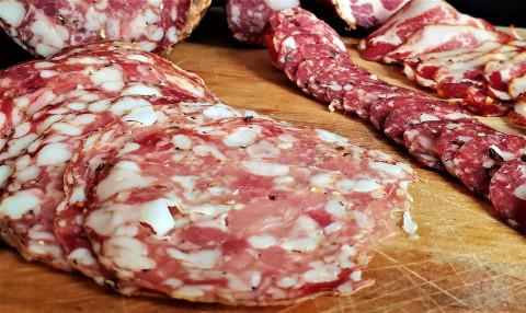 Sliced cured meats with specks of fat, arrayed on a wooden cutting board, offering a tempting array for charcuterie enthusiasts to buy salami.
