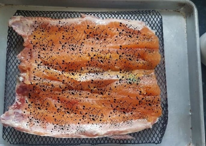 A tray of seasoned salmon fillets ready to be cooked, sprinkled with herbs or spices.