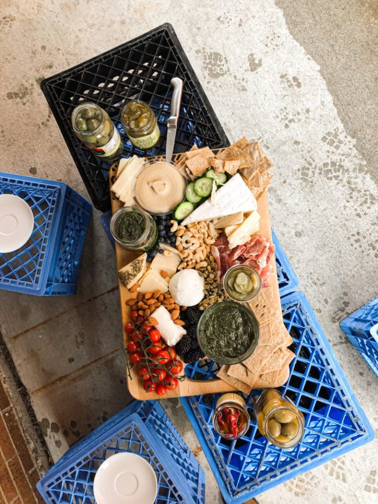 A top-down view of an elaborate charcuterie board arranged on a wooden serving tray, featuring a variety of cheeses, crackers, nuts, cured meats and accompaniments like dips and olives,