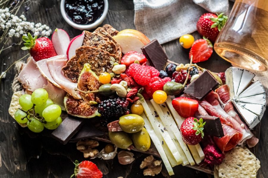 A lavish charcuterie board filled with an assortment of fresh fruits like strawberries and grapes, cured meats, assorted cheeses, nuts, and olives, perfect for gourmet feast essentials.