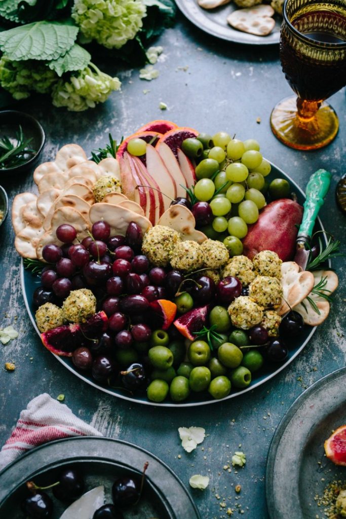 A colorful and appetizing charcuterie board, featuring an assortment of grapes, sliced apples, cheese, cured meat, and crackers, artfully arranged on a dark background, ready for a gourmet sn