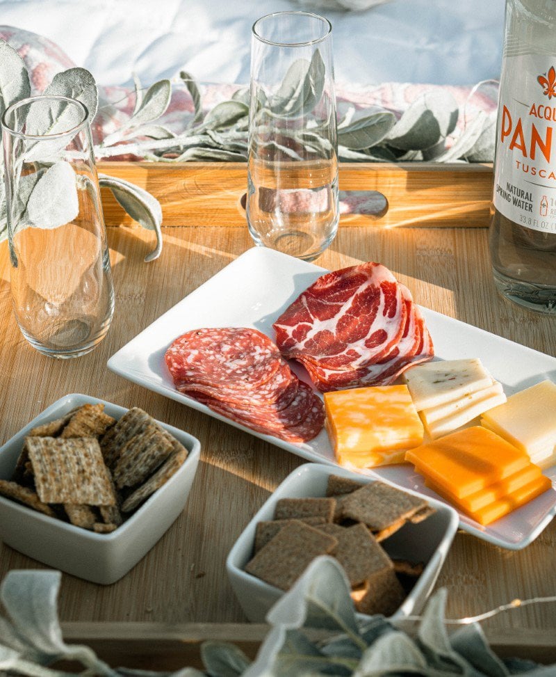 A delightful charcuterie board arrangement with an assortment of cheeses, cured meats, and crackers, ready for a relaxing and savory picnic experience.
