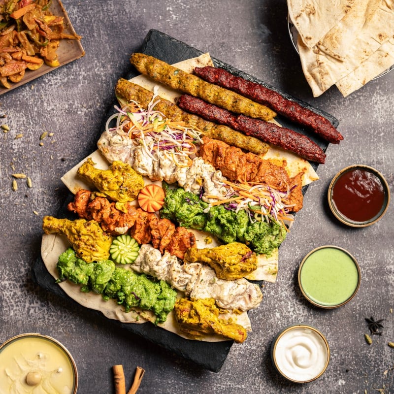 An enticing charcuterie board featuring middle eastern kebabs and an assortment of flavorful dips, showcasing a delicious mix of spices, vibrant colors, and cured meat.