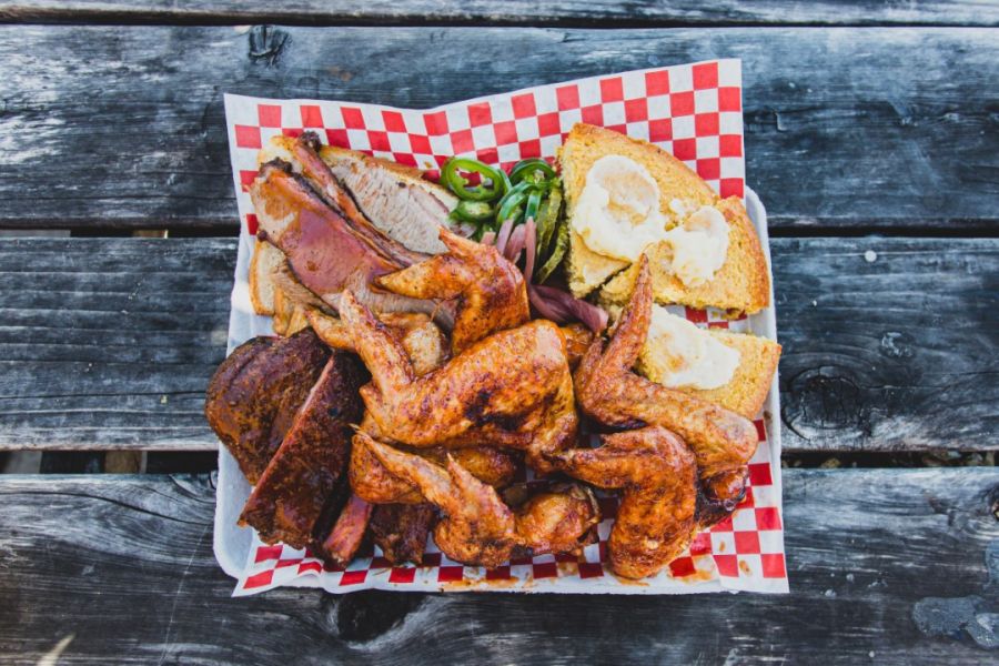 A hearty bbq feast with succulent smoked meats, including brisket and chicken wings, served with cornbread on a charcuterie board, ready to indulge the taste buds of barbecue enthusiasts.