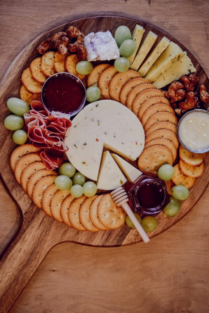 A delectable charcuterie board adorned with an assortment of crackers, essentials cured meats, nuts, and grapes, served with dips, presented beautifully on a wooden board. Perfect for an appetizer