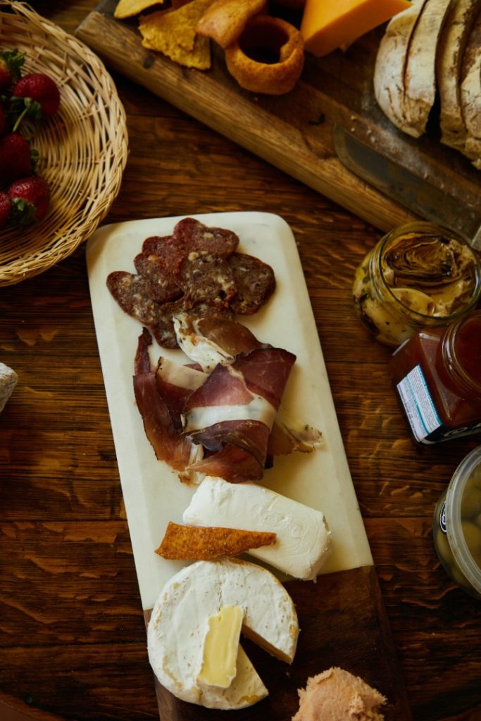 A rustic charcuterie board featuring an assortment of essentials such as cured meats, cheese, and bread, accompanied by strawberries and preserves on a wooden table, inviting a cozy and gourmet snacking experience.