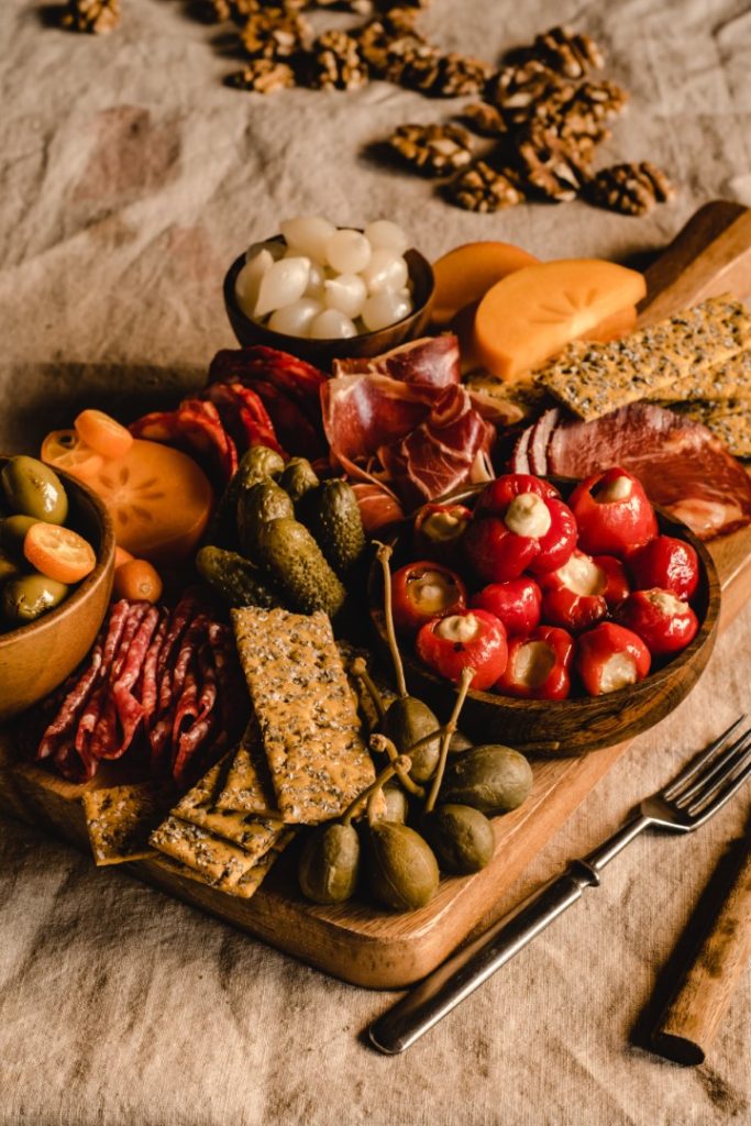 A rustic charcuterie board filled with an assortment of images & ideas, cheese-stuffed peppers, olives, pickles, and crackers, offering a variety of textures and flavors, beautifully arranged for