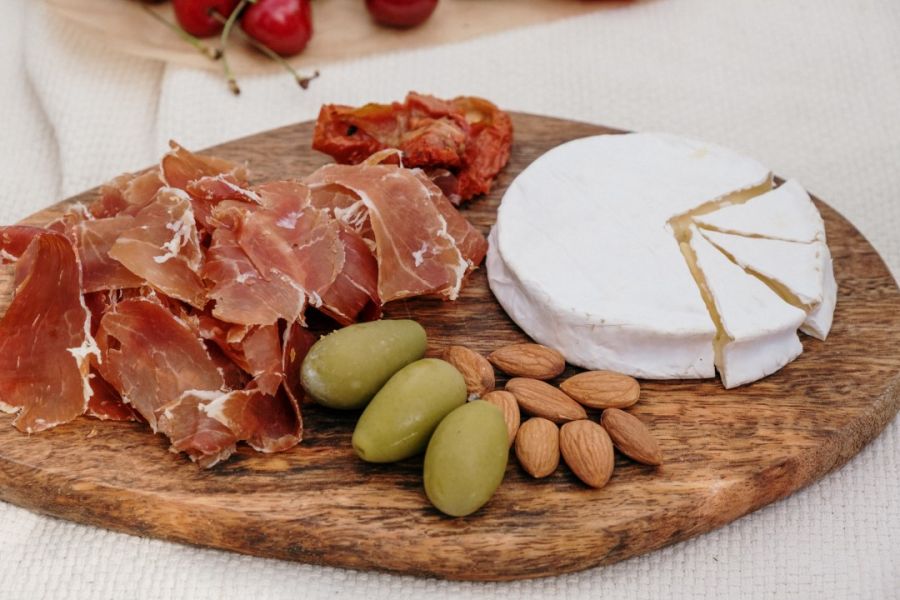 A delectable charcuterie board featuring thinly sliced cured meat, a creamy wheel of brie cheese with a wedge removed, green olives, almonds, and sun-dried tomatoes, artfully